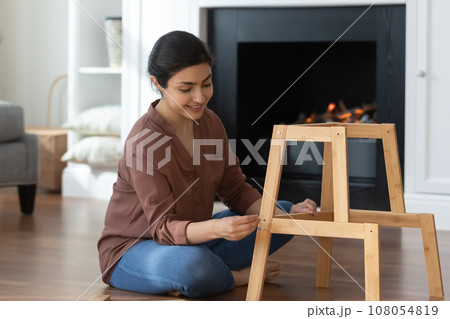 Happy Indian woman assembling new wooden furniture at home Happy Indian woman assembling new wooden furniture at home 108054819