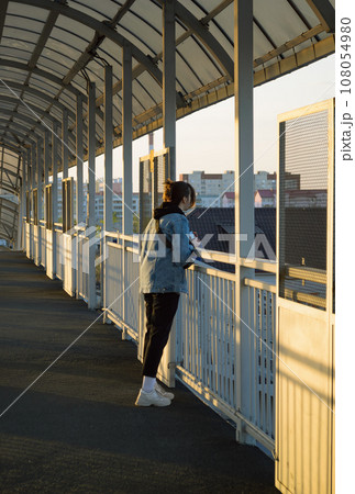 A girl in a denim jacket leans on the railing of a pedestrian bridge and looks into the distance A girl in a denim jacket leans on the railing of a pedestrian bridge and looks into the distance 108054980