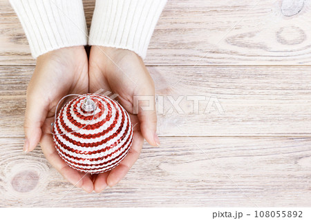 Christmas concept with hand and white ball - christmas tree toy. White round christmas ball in female hand. Wooden Background Christmas concept with hand and white ball - christmas tree toy. White round christmas ball in female hand. Wooden Background 108055892