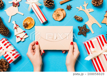 Top view of woman holding an envelope on blue background made of holiday decorations. Christmas time concept 108056020