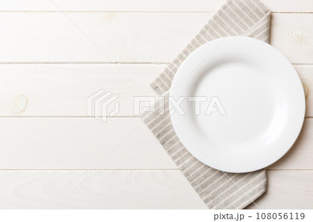 Top view on colored background empty round white plate on tablecloth for food. Empty dish on napkin with space for your design Top view on colored background empty round white plate on tablecloth for food. Empty dish on napkin with space for your design 108056119