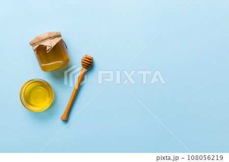 Glass jar of honey with wooden drizzler on colored background. Honey pot and dipper high above. Top view copy space Glass jar of honey with wooden drizzler on colored background. Honey pot and dipper high above. Top view copy space 108056219