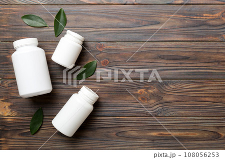 supplement pills with medicine bottle health care and medical top view. Vitamin tablets. Top view mockup bottle for pills and vitamins with green leaves, natural organic bio supplement, copy space 108056253