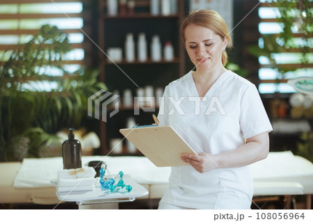 female massage therapist in massage cabinet with clipboard 108056964