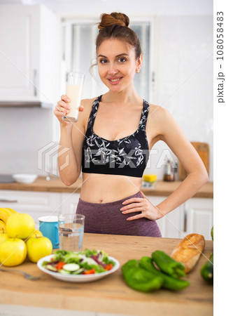 Positive young woman drinking dairy product at home 108058483