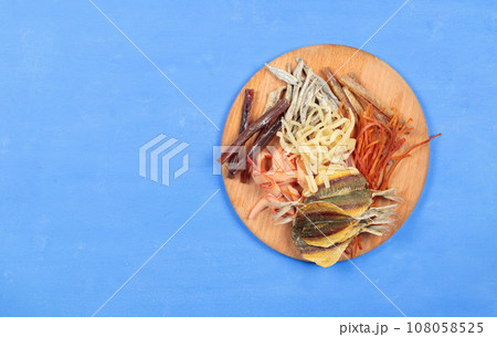 Snack board with dried and salted fish and squid. Top view on blue background, copy space. Snack board with dried and salted fish and squid. Top view on blue background, copy space. 108058525