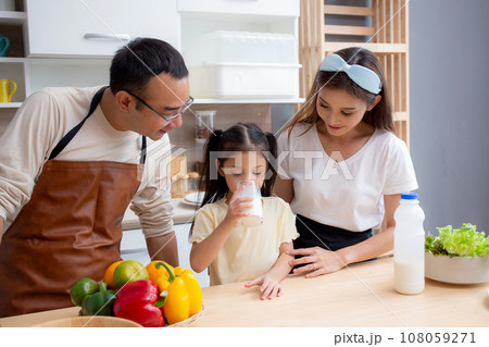 Happy family with father, mother and daughter in kitchen drinking milk in glass for healthy together 108059271