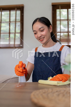 Asian woman wear rubber protective orange gloves sit clean guest reception desk with product and equipment cleaner at home 108060166