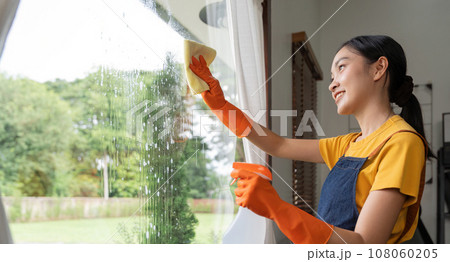 Young Asian housewife cleaning window glass with rags and detergent spray, cleaning house on the weekend Young Asian housewife cleaning window glass with rags and detergent spray, cleaning house on the weekend 108060205