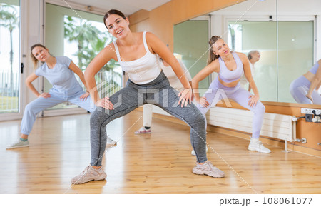 Excited sportive women of different ages dancing with legs wide apart in modern class of school for adults 108061077