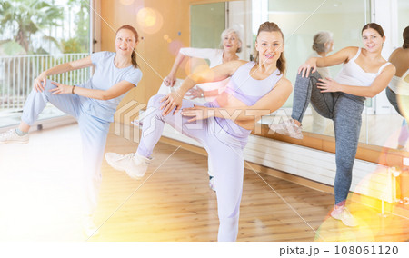 Group of energetic young mature female dancers dancing with knee lift during training together in dance hall Group of energetic young mature female dancers dancing with knee lift during training together in dance hall 108061120