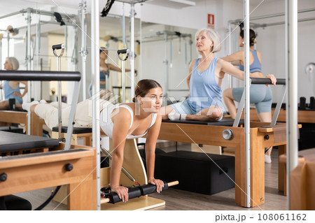 Young girl practicing pilates stretching exercises on combo chair Young girl practicing pilates stretching exercises on combo chair 108061162
