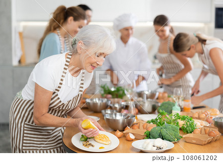 Mature woman decorating cooked chicken breast with mustard 108061202