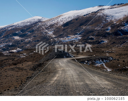 Mountain track off-road to a high-mountain village. Snow-covered narrow mountain road on the slope of snow mountains. Dangerous off-road driving along the mountains to the edge and steep cliffs. Mountain track off-road to a high-mountain village. Snow-covered narrow mountain road on the slope of snow mountains. Dangerous off-road driving along the mountains to the edge and steep cliffs. 108062185