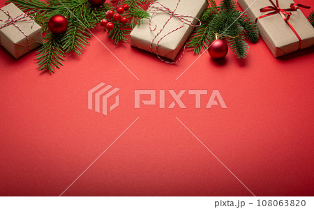 Christmas or New Year celebration red paper festive background with decoration fir tree, wrapped present boxes, cones, berries, sparkly red balls. Space for text. 108063820