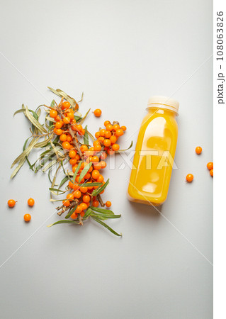 Sea buckthorn healthy juicy drink in bottle and branches with leaves and ripe berries top view on light grey simple background. 108063826