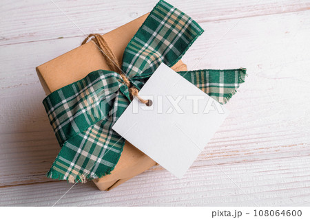 Christmas square gift tag mockup with craft wrapped gift box on a white background 108064600