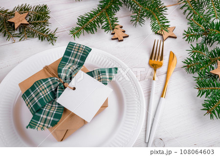Christmas table setting with gift box and square gift tag mockup on white plate and golden cutterly 108064603