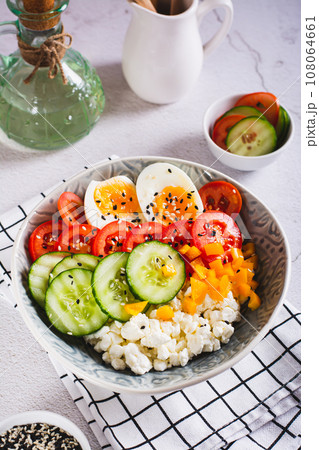 Cottage cheese, fresh vegetables, boiled egg and sesame seeds in a bowl on the table vertical view Cottage cheese, fresh vegetables, boiled egg and sesame seeds in a bowl on the table vertical view 108064661