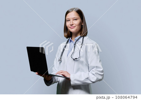 Young woman doctor, medical student with laptop on grey background Young woman doctor, medical student with laptop on grey background 108064794