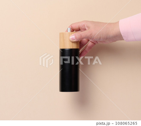 Female hand holding a wooden pepper mill on a beige background 108065265