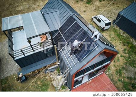 Electricians connecting cables while installing photovoltaic solar panels on roof of house. Aerial view of mounters mounting of PV solar module on rooftop. Concept of alternative and renewable energy. 108065429