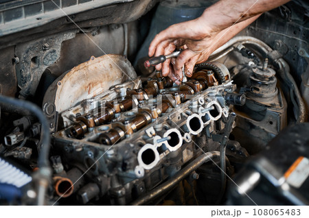 Close up of mechanic repairing car engine, working in garage, workshop, auto servicing center. Worker, repairman holding screwdriver. Concept of fixing car. 108065483