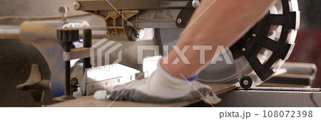 Man in protective gloves works with miter saw cutting board Man in protective gloves works with miter saw cutting board 108072398