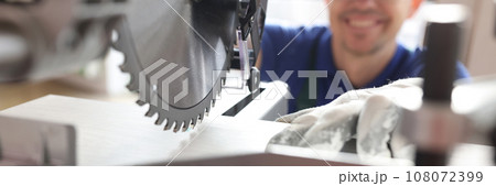 Smiling worker in cap cuts wooden board with miter saw Smiling worker in cap cuts wooden board with miter saw 108072399