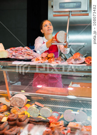 Young woman butchery worker weighing sausage Young woman butchery worker weighing sausage 108073482