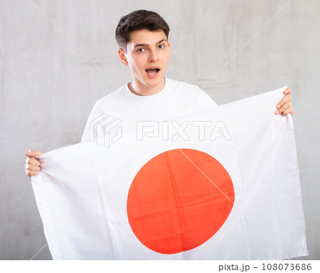 Energized, active male spectator holds national flag of Japan in hands and chants popular slogan. 108073686