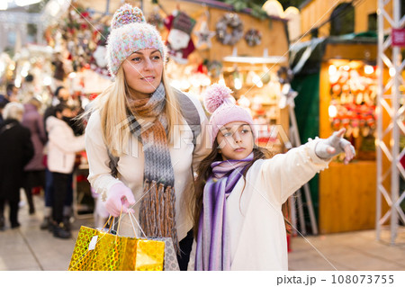 Smiling woman with tweenage daughter pointing to something while choosing decorations on traditional market 108073755
