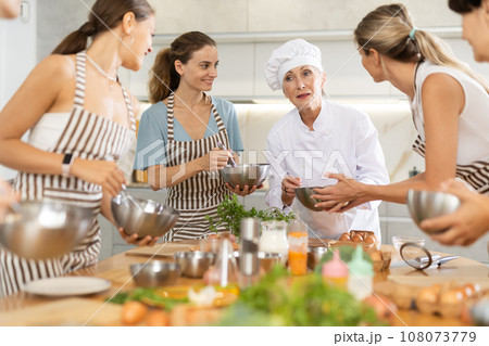 Mature female cook holding bowl and whisk 108073779