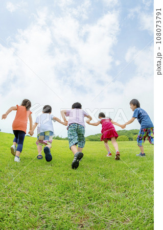 公園の丘を手をつないで駆け上がる小学生たちの後ろ姿 公園の丘を手をつないで駆け上がる小学生たちの後ろ姿 108073791