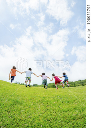 公園の丘を手をつないで駆け上がる小学生たちの後ろ姿 公園の丘を手をつないで駆け上がる小学生たちの後ろ姿 108073795