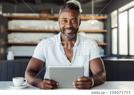 Cheerful African American man in casual clothes with tablet and cup of coffee sitting in cafe. Smiling mature man, successful entrepreneur or employee working online. Remote work concept. 108075755
