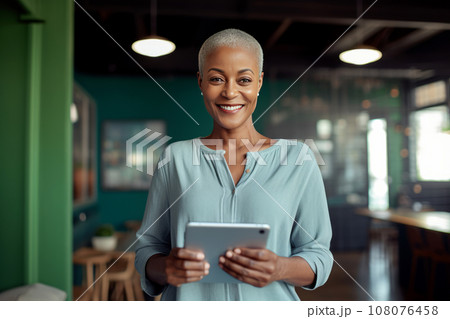 Portrait of cheerful African American woman in casual clothes holding a tablet or smartphone in cafe. Happy smiling young lady, successful entrepreneur or employee works online. Remote work concept. 108076458