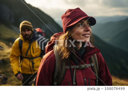 Happy young couple of tourists against the backdrop of stunning mountain landscape. Cheerful hikers in modern bright outfits with backpacks walking along mountain path. Active sports and travel. 108076499