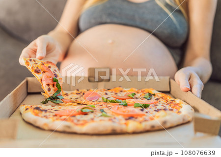 A pregnant woman enjoys a slice of pizza, savoring a moment of indulgence while satisfying her craving for a delightful, comforting treat. Excited Pregnant Young Lady Enjoying Pizza Holding Biting A pregnant woman enjoys a slice of pizza, savoring a moment of indulgence while satisfying her craving for a delightful, comforting treat. Excited Pregnant Young Lady Enjoying Pizza Holding Biting 108076639