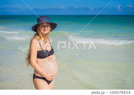 Radiant pregnant woman in a swimsuit, amid the stunning backdrop of a turquoise sea. Serene beauty of maternity by the shore 108076658