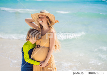 A radiant pregnant mother and her excited son share a tender moment on a serene, snow-white beach, celebrating family love amidst nature's beauty A radiant pregnant mother and her excited son share a tender moment on a serene, snow-white beach, celebrating family love amidst nature's beauty 108076697