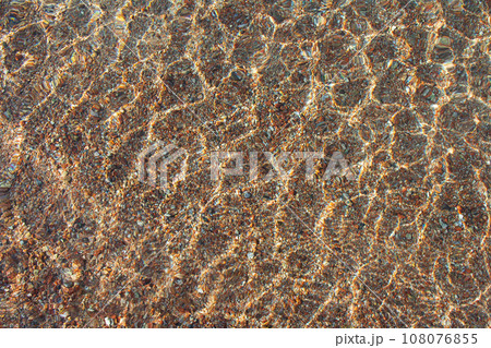 Transparent texture of sea, lake surface of clear water with ripples above sandy pebble bottom. Abstract summer background. Copy space Transparent texture of sea, lake surface of clear water with ripples above sandy pebble bottom. Abstract summer background. Copy space 108076855