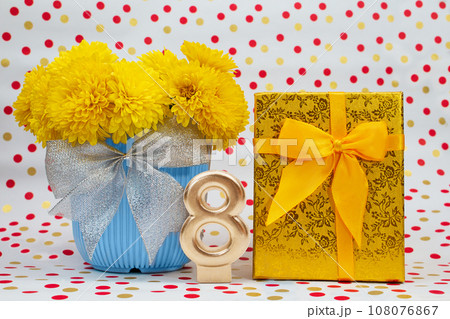 Bouquet of yellow chrysanthemums in blue pot with bow and golden gift box, number 8, behind white background with polka dots. International Women's Day, March 8, birthday Bouquet of yellow chrysanthemums in blue pot with bow and golden gift box, number 8, behind white background with polka dots. International Women's Day, March 8, birthday 108076867