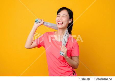 Portrait young asian sports fitness woman happy smile wearing pink sportswear and face towel doing exercise training workout against yellow studio background. wellbeing and healthy lifestyle concept. 108080878