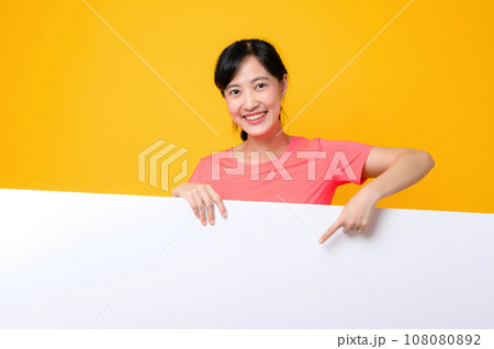 young asian sports fitness woman happy smile wearing pink sportswear standing behind the white blank banner or empty space advertisement board against yellow background. wellbeing lifestyle concept. young asian sports fitness woman happy smile wearing pink sportswear standing behind the white blank banner or empty space advertisement board against yellow background. wellbeing lifestyle concept. 108080892