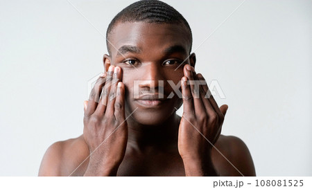 Man care. Facial treatment. Wrinkles skincare. Confident shirtless guy applying rejuvenation face skin cream under eyes isolated on white background. Man care. Facial treatment. Wrinkles skincare. Confident shirtless guy applying rejuvenation face skin cream under eyes isolated on white background. 108081525