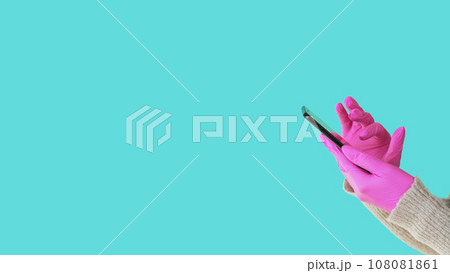 Mobile using. Quarantine ordering. Unrecognizable human hands in protective gloves holding smartphone browsing internet isolated on blue empty space background. Mobile using. Quarantine ordering. Unrecognizable human hands in protective gloves holding smartphone browsing internet isolated on blue empty space background. 108081861