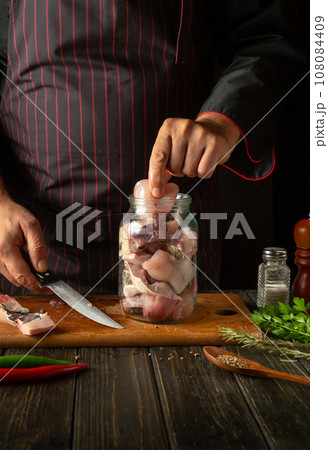 The chef puts steaks with raw fish into a jar. The concept of salting or canning fish at home with spices and coriander at home The chef puts steaks with raw fish into a jar. The concept of salting or canning fish at home with spices and coriander at home 108084409
