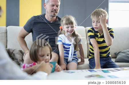 Man and children are sitting on couch next to table with playing cards laid out 108085610