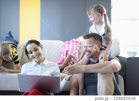 Man and woman and their children are smiling and laughing while sitting on floor and looking at laptop. 108085630